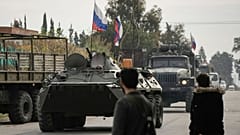 DATEI - Syrische Kämpfer beobachten russische Panzerfahrzeuge, die in der Nähe des syrischen Luftwaffenstützpunkts Hmeimim vorbeifahren, der derzeit von Russland betrieben wird, 16. Dezember 2024. 