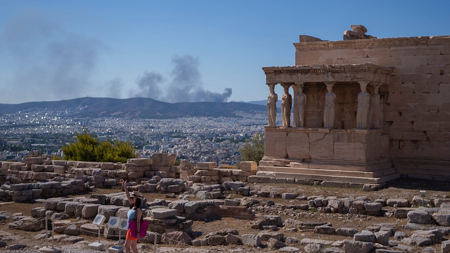 Una donna posa per una foto davanti alle statue delle Cariatidi che sorreggono il portico del tempio Eretteo di Atene, risalente al V secolo a.C..