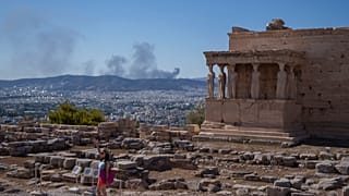 A woman poses for a photo in front Caryatid statues that prop up the porch of the 5th century B.C. Erechtheion temple in Athens.
