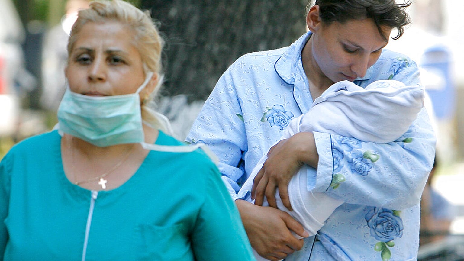 A woman of the medical staff with a mask leads a patient holding a baby at the Matei Bals hospital in Bucharest, Romania, Wednesday, May 27 2009