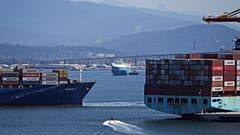FILE - A boater passes between cargo ships on the harbour, in Vancouver, British Columbia, July 16, 2024. (Darryl Dyck/The Canadian Press via AP, File)