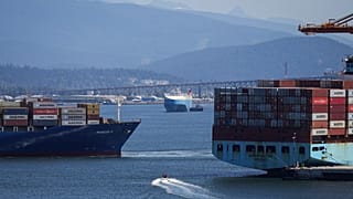 FILE - A boater passes between cargo ships on the harbour, in Vancouver, British Columbia, July 16, 2024. (Darryl Dyck/The Canadian Press via AP, File)