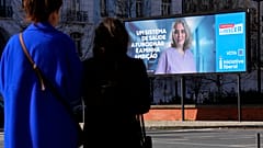 Pessoas passam por um cartaz de campanha eleitoral do partido político Iniciativa Liberal em Lisboa, segunda-feira, 26 de fevereiro de 2024