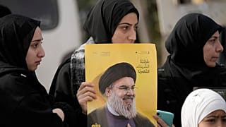 امرأة لبنانية تحمل صورة الأمين العام لحزب الله حسن نصر الله، أثناء انتظارها مع آخرين للحصول على إذن من الجيش اللبناني لدخول قريتهم، في بنت جبيل جنوب لبنان، الأحد 26 يناير 2025