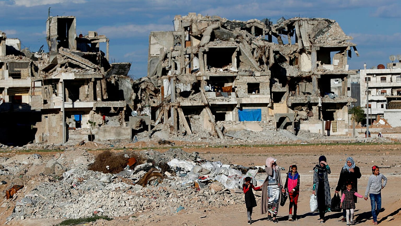 ARQUIVO: Cidadãos sírios caminham em frente a edifícios que foram destruídos em Manbij, no norte da Síria, a 31 de março de 2018.