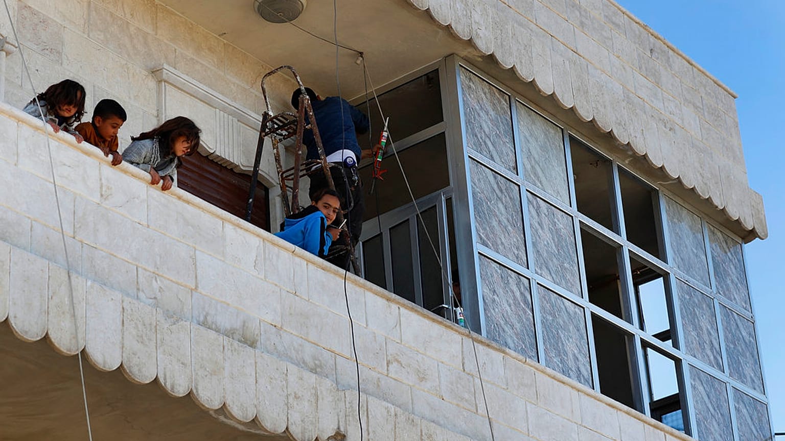 Des enfants syriens se tiennent sur le balcon de leur maison tandis que leur père répare les fenêtres endommagées, sur les lieux où une explosion à Manbij
