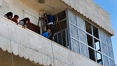 Des enfants syriens se tiennent sur le balcon de leur maison tandis que leur père répare les fenêtres endommagées, sur les lieux où une explosion à Manbij
