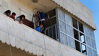 Des enfants syriens se tiennent sur le balcon de leur maison tandis que leur père répare les fenêtres endommagées, sur les lieux où une explosion à Manbij
