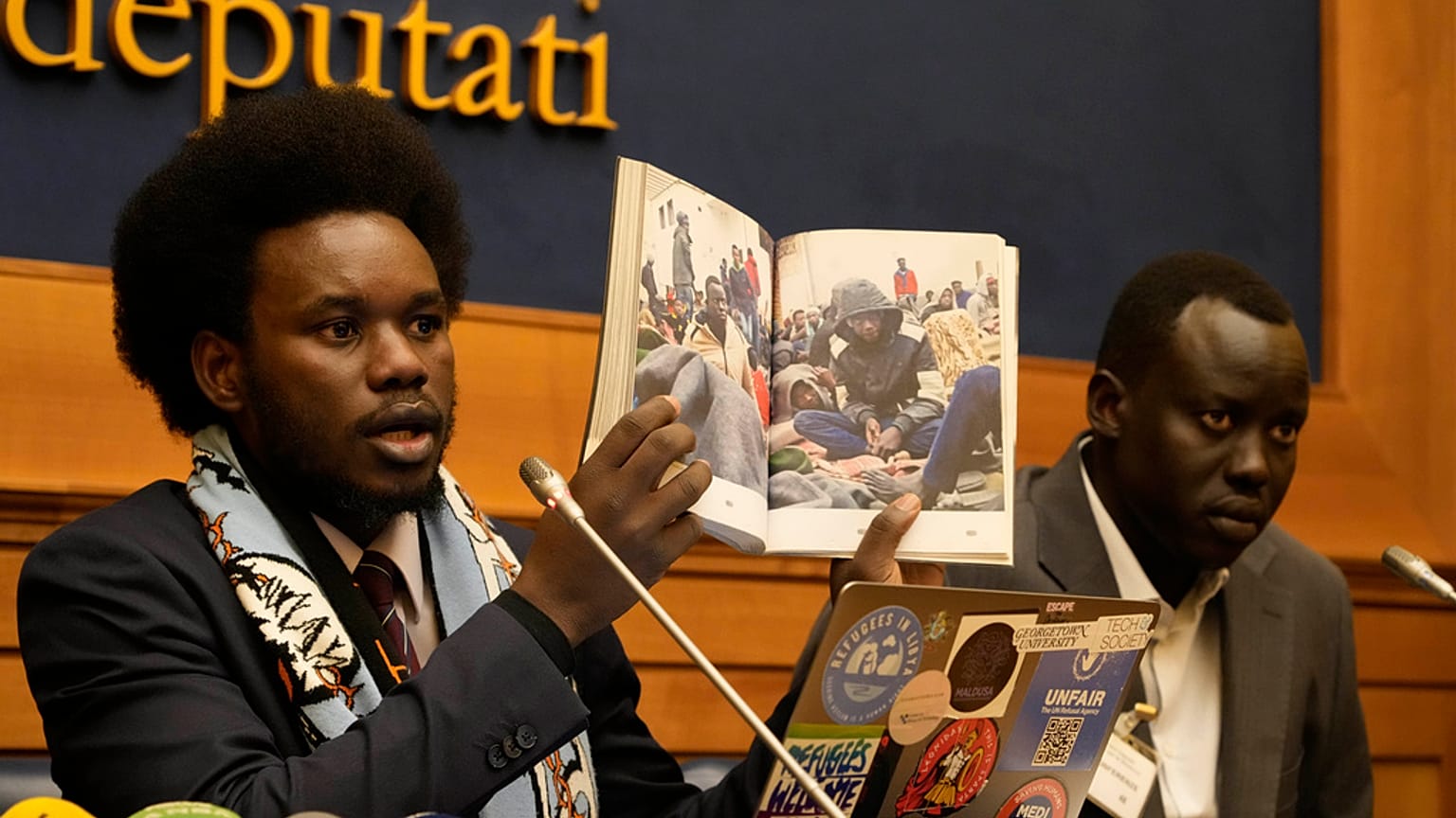 David Yambio, a sinistra, affiancato da Lam Magok, entrambi del Sud Sudan, mostra una foto di migranti detenuti in un carcere libico durante una conferenza stampa alla Camera 