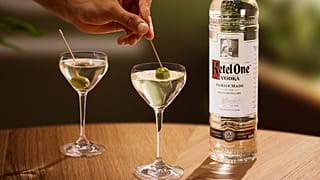 A bottle of Ketel One vodka and two dirty martinis on a table.