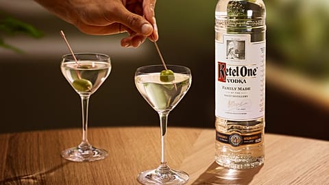 A bottle of Ketel One vodka and two dirty martinis on a table. 