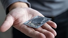 Ein Mann hält ein Kondom in der Hand.