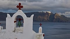 Eine orthodoxe Kirche in der Stadt Oia auf Santorin, Griechenland, während der Hauptort Fira im Hintergrund von der Sonne beleuchtet wird, am 4. Februar 2025.