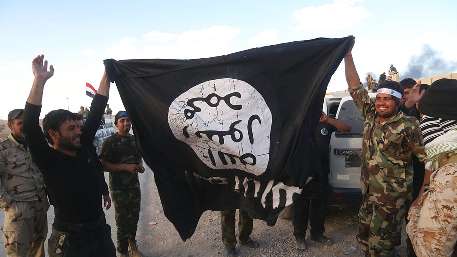  In this Tuesday, March 31, 2015 file photo, Iraqi security forces and allied Shiite militiamen celebrate as they hold a flag of the Islamic State.