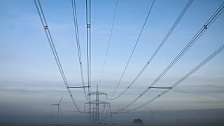 Wind turbines stand next to electricity pylons in the morning fog near Muencheberg, Germany, Thursday, Oct. 28, 2021.