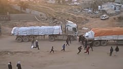 Les personnes courent vers des camions, grimpent dessus et prennent des cartons contenant de la nourriture.