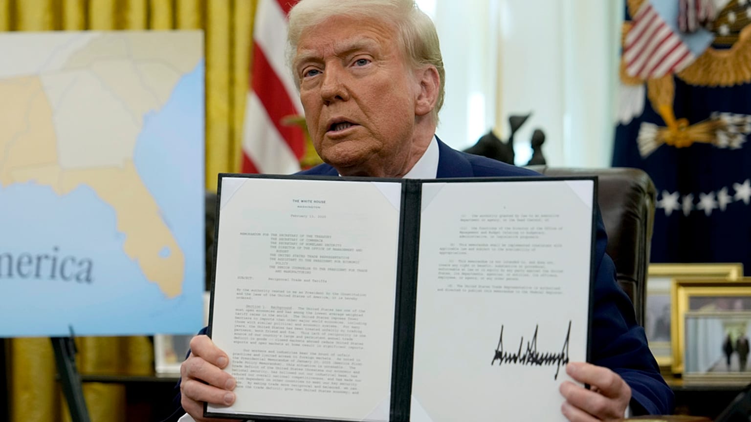 President Donald Trump holds up a signed executive order in the Oval Office of the White House, Thursday, Feb. 13, 2025, in Washington.
