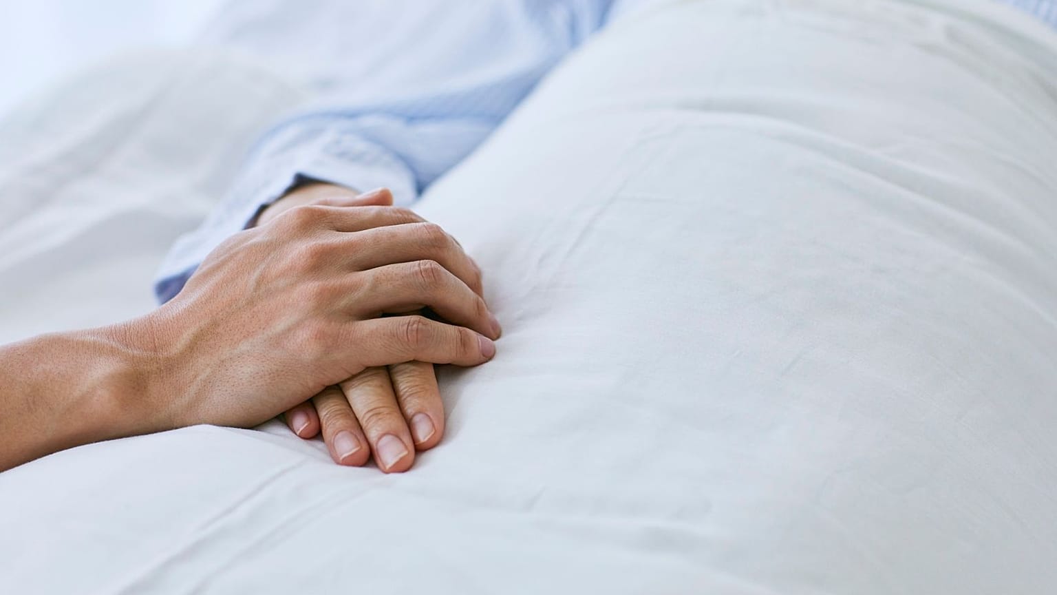 A visitor holds the patient's hand in a hospital.