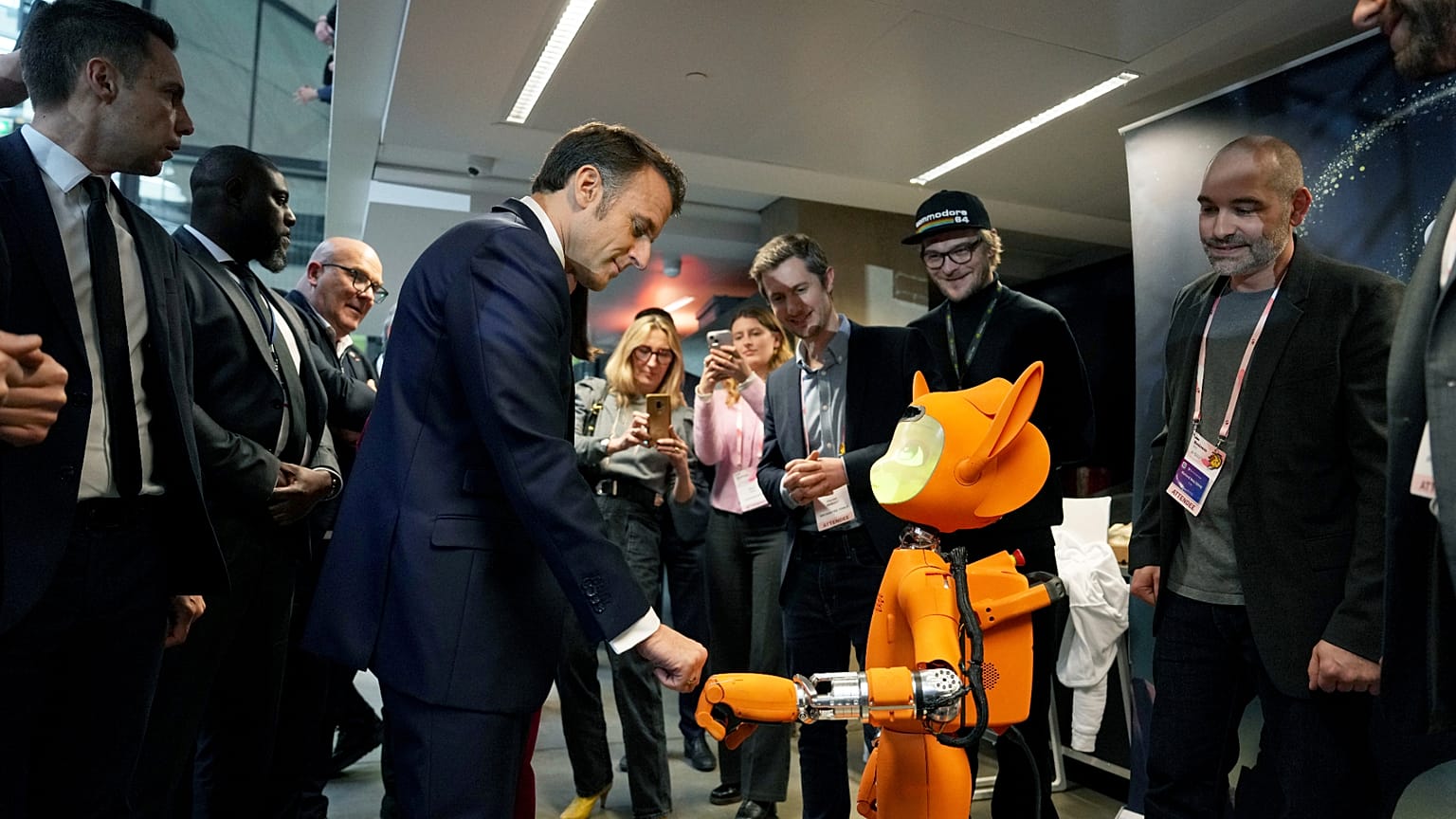 Prezydent Francji Emmanuel Macron, w środku po lewej, uderza pięścią robota podczas wizyty w Station F, w ramach wydarzenia na marginesie Artificial Intelligence Action.