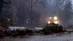 Mud flows down a road during a flash flood in front of a bulldozer clearing debris in the Eaton Fire zone during a storm Thursday, Feb. 13, 2025, in Altadena, Calif. 