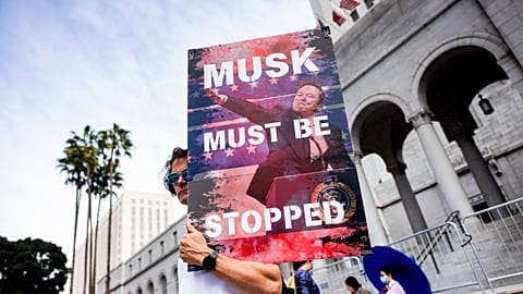 A demonstrator holds a poster of Elon Musk during a rally to protest President Trump's policies on Presidents Day on Monday