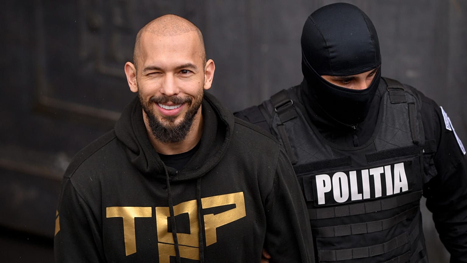 ملف: ضابط شرطة يصطحب أندرو تيت، في الوسط، مكبل اليدين من محكمة الاستئناف في بوخارست، 12 مارس/آذار 2024