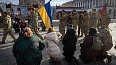 Persone si inginocchiano mentre i soldati trasportano la bara di un soldato volontario a Kiev (30 gennaio 2025)