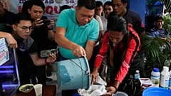 Köy muhtarı Carlito Cernal, ortada, Filipinler'in Mandaluyong şehrinde bir köy sakini tarafından yakalanan sivrisinek larvalarının bulunduğu bir kabı döküyor, 19 Şubat 2025