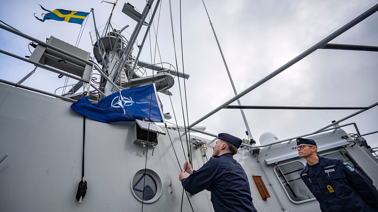 Kapitan Thomas Zimmerman, po prawej, wydaje rozkaz podniesienia flagi NATO na okręcie patrolowym HMS Carlskrona (P04) wypływającym z portu marynarki wojennej w Karlskronie w Szwecji.