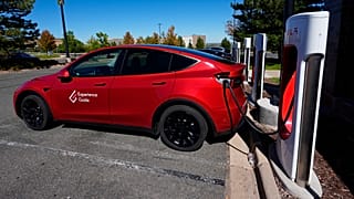 A Tesla Model 3 charges at a Tesla supercharging station in a parking lot in Lakewood, Colorado.