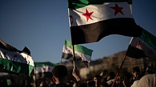 Sírios agitam bandeiras "revolucionárias" da Síria durante uma manifestação comemorativa após as primeiras orações de sexta-feira desde a destituição de Bashar Assad, na praça central de Damasco, Síria