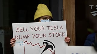 A protestor holding a sign outside a Tesla showroom in Seattle