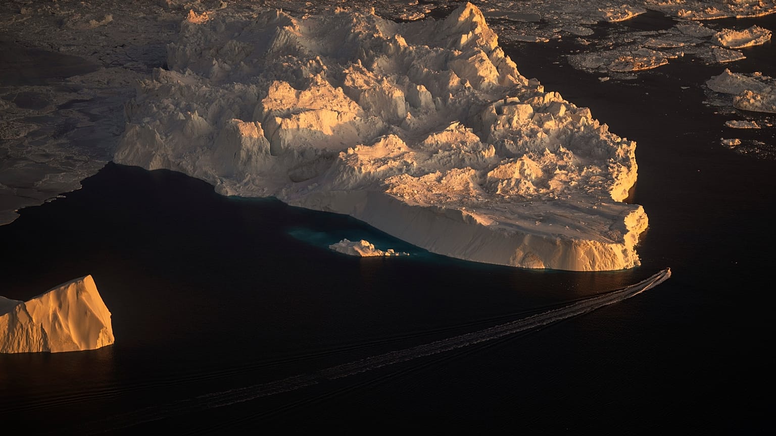  Ein Schiff fährt entlang eines großen Eisbergs in Ilulissat, Grönland.