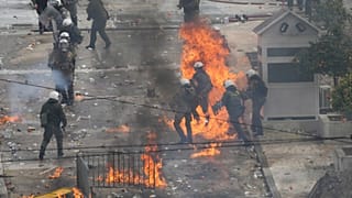 Fuerzas policiales griegas intentan evitar los cócteles molotov lanzados por encapuchados frente al Parlamento durante la concentración para conmemorar los dos años de la tragedia de Tempi.