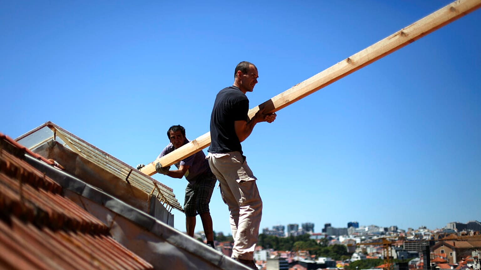 onstruction workers stand on the roof of a building in downtown Lisbon, Friday, Aug. 9, 2013.