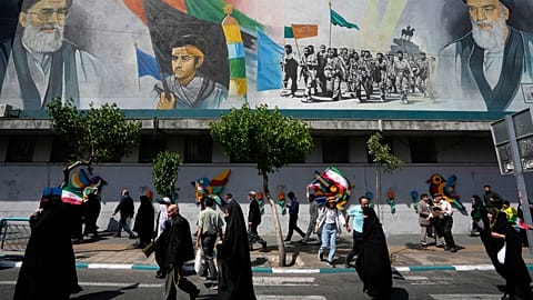 Iranian worshippers walk past a mural showing the late revolutionary founder Ayatollah Khomeini, right, Supreme Leader Ayatollah Ali Khamenei, left, and Basij paramilitary for