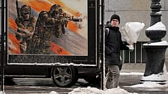 Ein Mann trägt einen Blumenstrauß, als er am 14. Februar 2025 in St. Petersburg an einer Straßenausstellung mit Militärpostern der russischen Armee vorbeigeht.