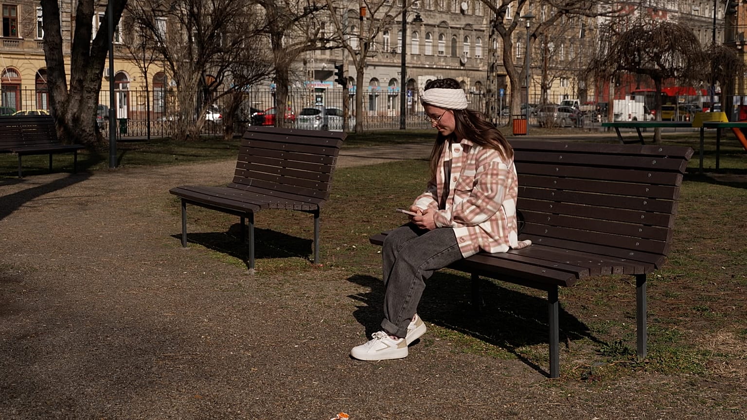 Egy kárpátaljai menekült, Kenéz Andrea nézi a telefonját egy budapesti parkban