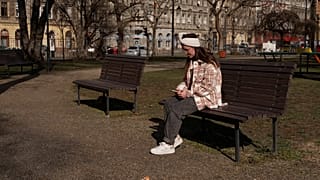 Egy kárpátaljai menekült, Kenéz Andrea nézi a telefonját egy budapesti parkban