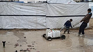 Imagen de dos palestinos que transportan agua en bidones en un campamento improvisado para desplazados en un barrio de la ciudad de Gaza, el 7 de marzo de 2025.
