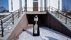 Priester Andriy steht während einer Gedenkfeier zum dritten Jahrestag der russischen Invasion in die Ukraine neben seiner Kirche in. Butscha.
