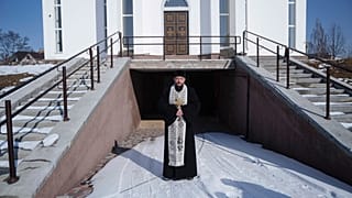 Andrij ortodox pap áll a temploma mellett Bucsában, a háború harmadik évfordulója alkalmából tartott megemlékezésen