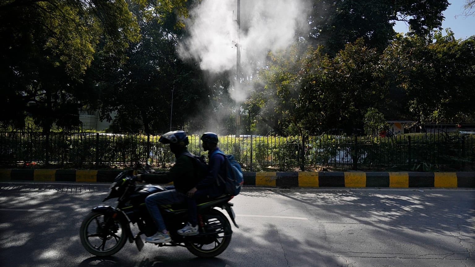 Bir motosiklet sürücüsü 12 Şubat 2025'te Yeni Delhi'de tozu dindirmek ve hava kirliliğini yatıştırmak amacıyla su püskürten fıskiyelerin yanından geçiyor.