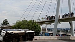 Bir köprü üzerinde duran yayalar, 11 Mart 2025 tarihinde Güney Afrika'nın Johannesburg kentinde otoyolda devrilen bir otobüse bakıyor. 