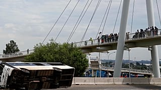Bir köprü üzerinde duran yayalar, 11 Mart 2025 tarihinde Güney Afrika'nın Johannesburg kentinde otoyolda devrilen bir otobüse bakıyor. 