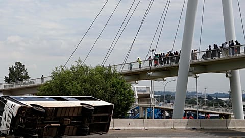 Pedestrians standing on a bridge look at a bus that overturned on a highway in Johannesburg, South Africa, on 11 March, 2025. 