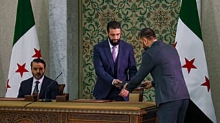 Il presidente ad interim della Siria Ahmad Al-Sharaa, al centro, si prepara a firmare una costituzione temporanea per il Paese a Damasco.