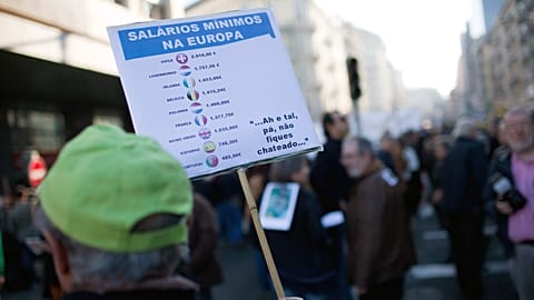 A man holds a sign with the minimum wage of different European countries during a protest against the government's austerity measures. Lisbon, 21 January 2012.