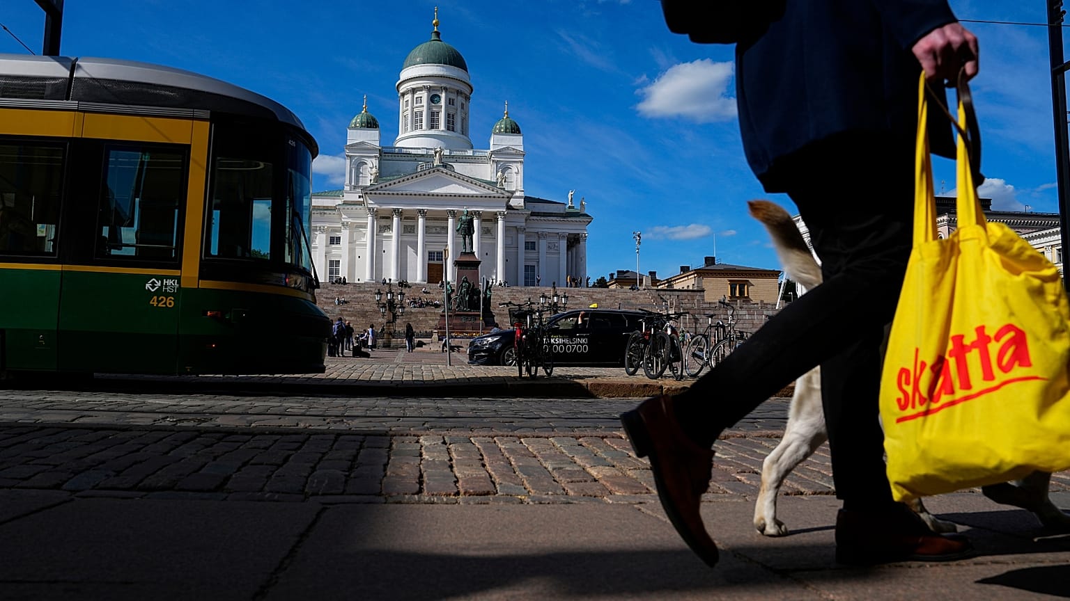 Una mujer pasea con un perro con la catedral de Helsinki al fondo.