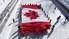Jugendliche laufen mit einer großen kanadischen Flagge auf dem Rideau Canal Schlittschuh, um die Feierlichkeiten zum 60. Jahrestag der kanadischen Nationalflagge zu eröffnen.